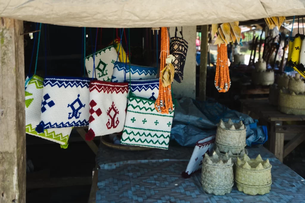 Wooden Sumbanese swords with curved handles are displayed in a wooden crate at a market, with textiles in the background.