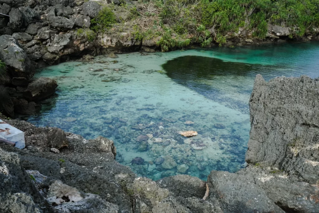 A clear turquoise lagoon is surrounded by gray rocks and green vegetation on Sumba Island, Indonesia.