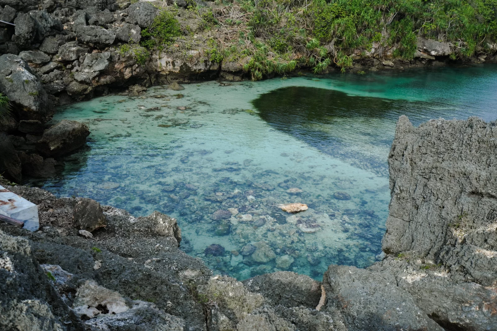 A clear turquoise lagoon is surrounded by gray rocks and green vegetation on Sumba Island, Indonesia.