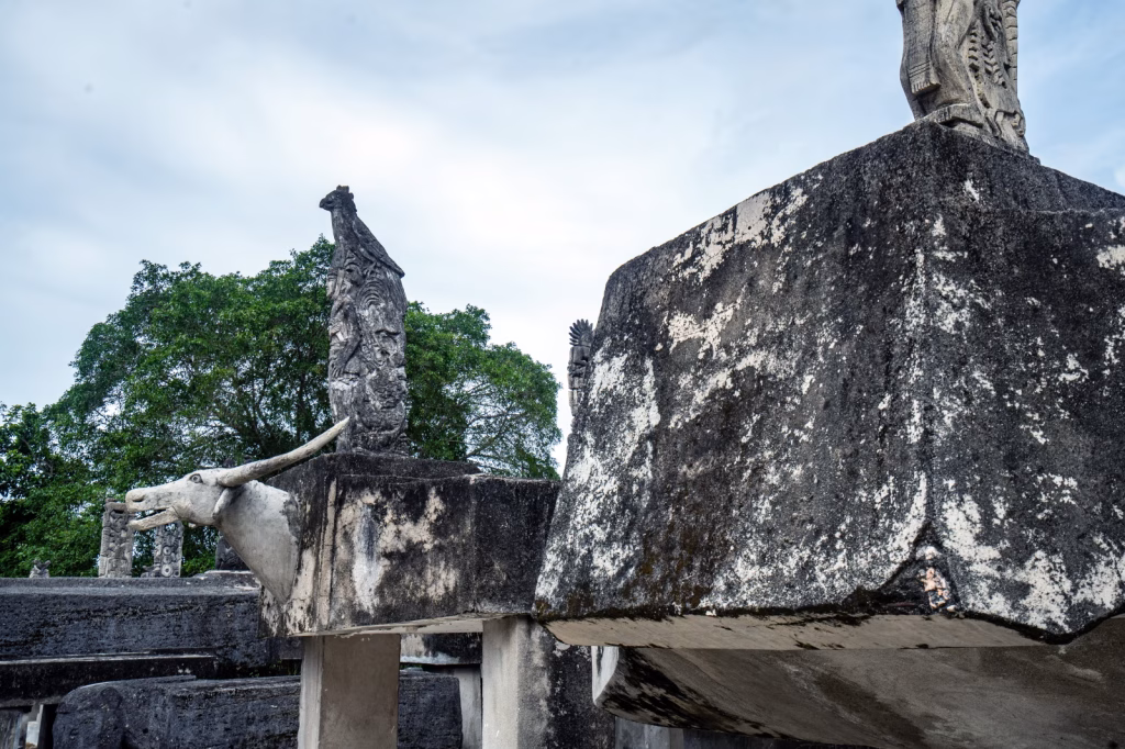 Stone carvings of animals and figures stand against a backdrop of green trees and a white sky in Sumba, Indonesia. Villages in Sumba.