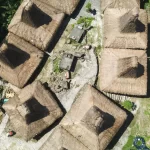 Aerial view shows traditional Sumba houses with high thatched roofs in a village setting, surrounded by green vegetation.