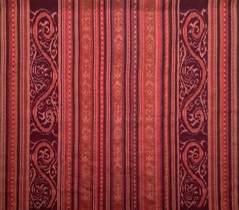 The image shows a textile with vertical stripes and intricate patterns in shades of red, brown, and purple.