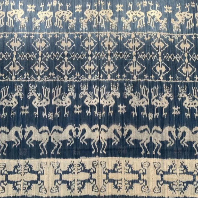 A blue and white textile displays traditional Sumba ikat patterns, including horses and geometric shapes.