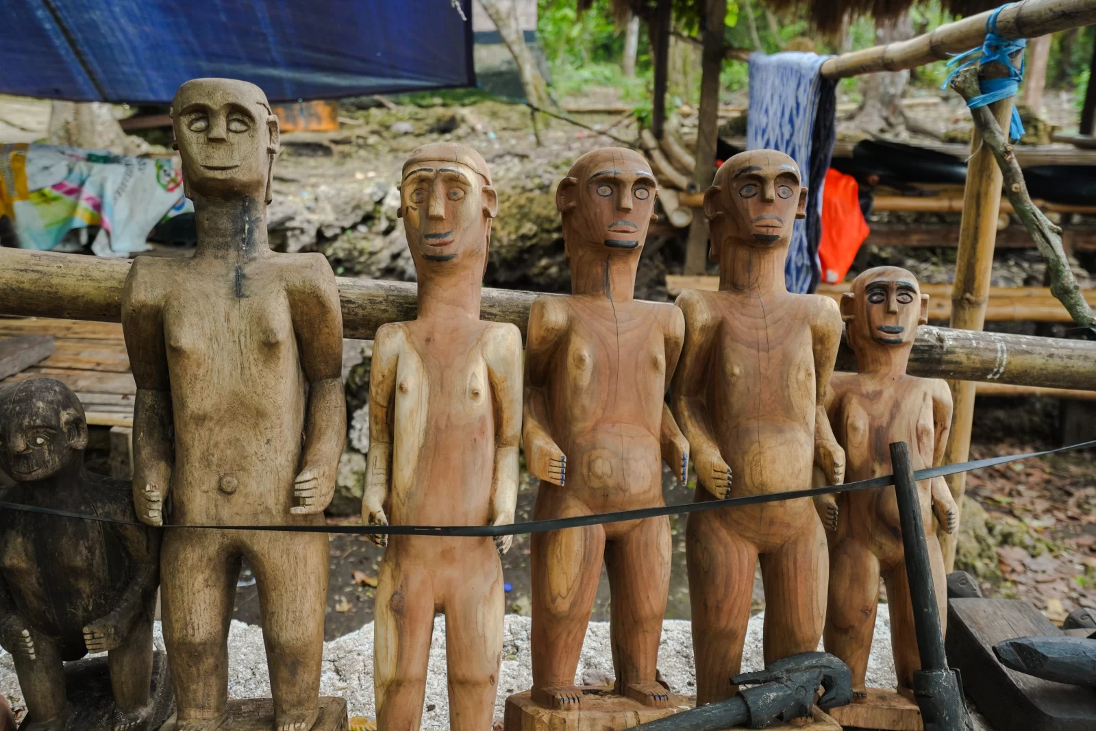 Six wooden statues of human figures stand in a row, varying in size and color from light tan to dark brown.