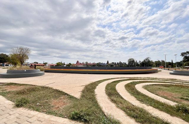 The Alun-Alun Kota Tambolaka city square features a large central sign, paved pathways, and green spaces under a cloudy sky.