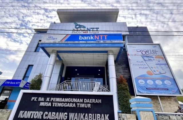 Blue and white Bank NTT building in Waikabubak, West Sumba, with an entrance and large bank signs, visible under a cloudy sky.