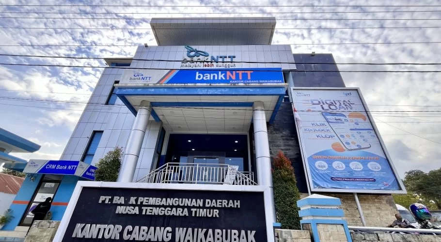 Blue and white Bank NTT building in Waikabubak, West Sumba, with an entrance and large bank signs, visible under a cloudy sky.