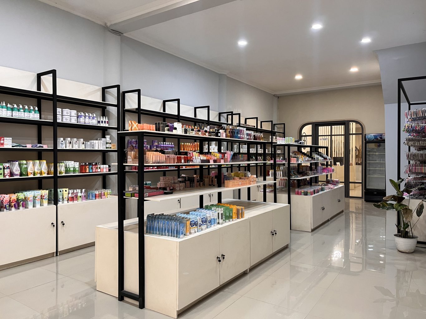 A bright, modern beauty store interior in Waingapu features black-framed shelves filled with colorful skincare and makeup products, with an arched doorway in the background.