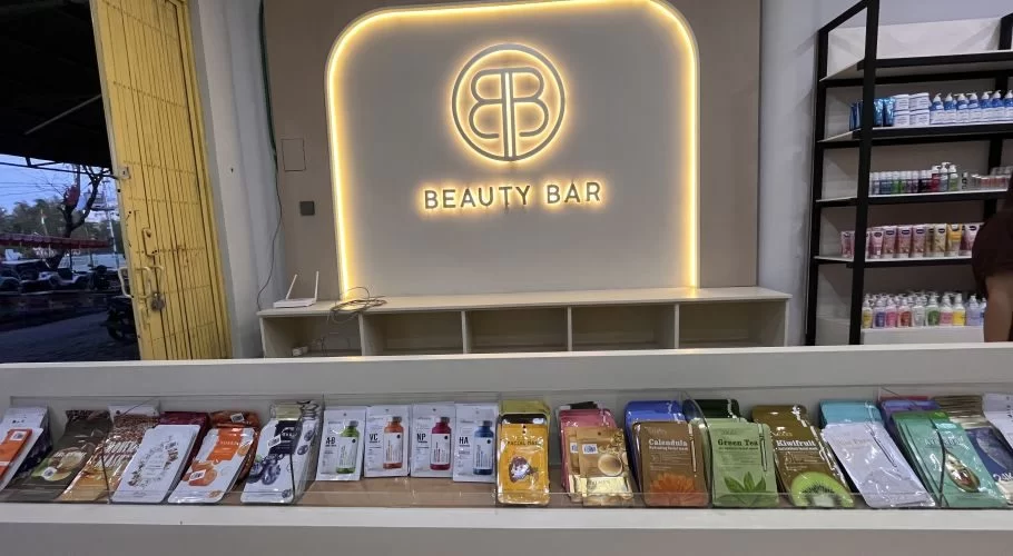 Inside the Beauty Bar store in Waingapu, a glowing 'BB' logo sign illuminates a counter filled with colorful skincare products and shelves.