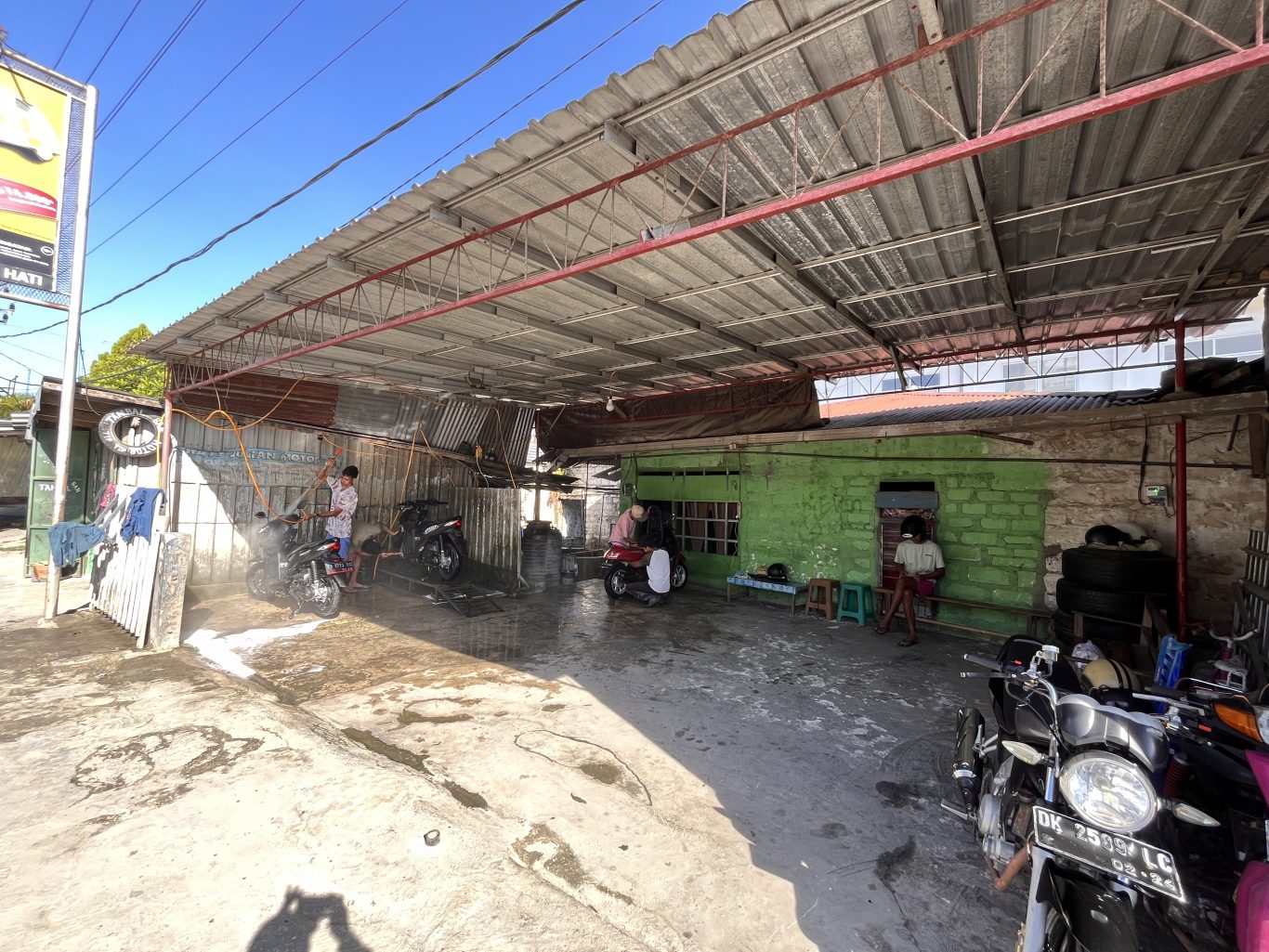 A worker sprays a motorcycle with water and foam at Cathy Julian Motor, an outdoor wash shop in Waikabubak, Sumba.