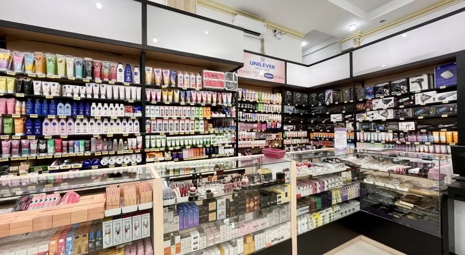 Visible is a brightly lit interior of a convenience store aisle, featuring shelves packed with colorful beauty, skincare, and personal care products.