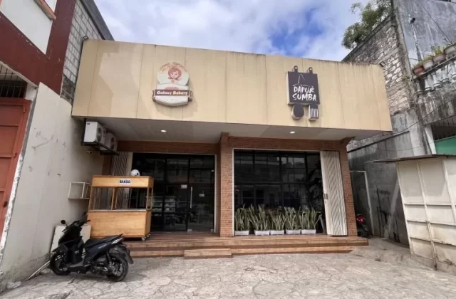 Exterior of Dapur Sumba restaurant in Waikabukak, Sumba, showing a light-colored building with glass windows and a bakso cart.