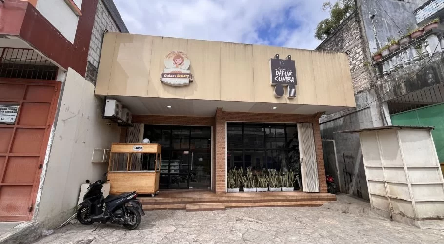 Exterior of Dapur Sumba restaurant in Waikabukak, Sumba, showing a light-colored building with glass windows and a bakso cart.