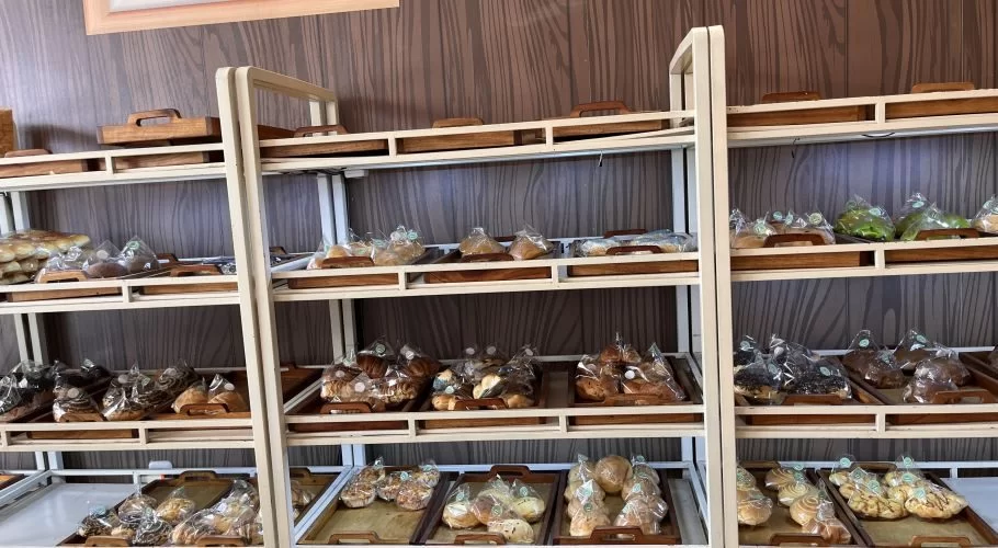 Visible are multiple shelves displaying various individually plastic-wrapped baked goods and pastries against a dark wood-paneled wall.