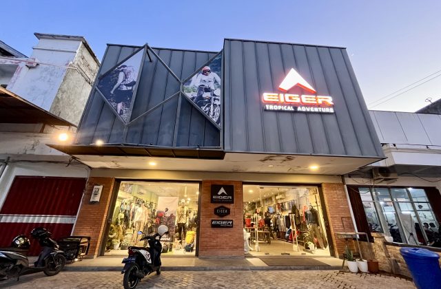 The Eiger outdoor gear store in Waingapu features a modern grey facade with a glowing orange logo, large display windows, and images of adventurers.