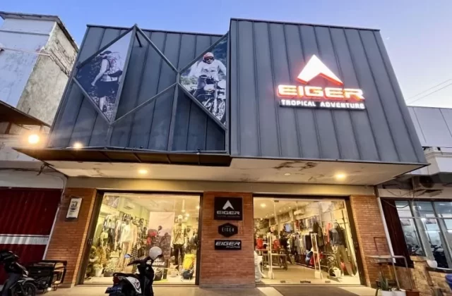 The Eiger outdoor gear store in Waingapu features a modern grey facade with a glowing orange logo, large display windows, and images of adventurers.