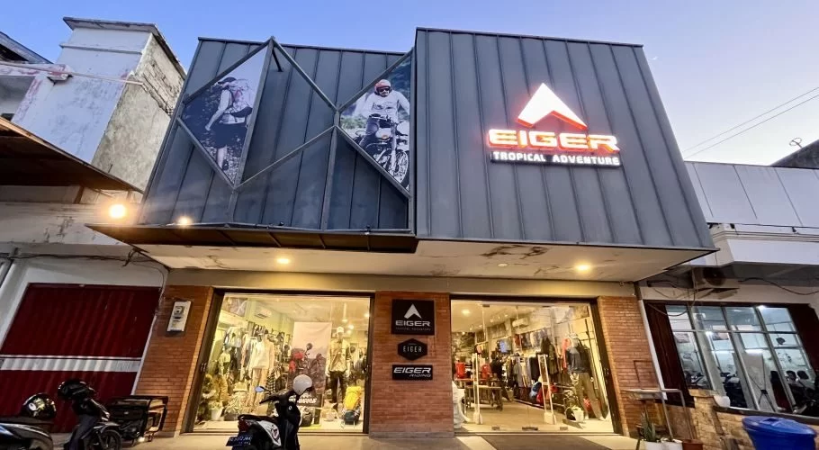 The Eiger outdoor gear store in Waingapu features a modern grey facade with a glowing orange logo, large display windows, and images of adventurers.