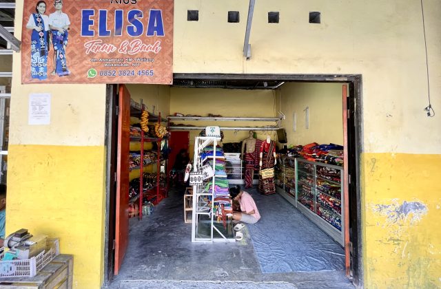 The entrance to Elisa Store reveals a person kneeling amidst vibrant Ikat Sumba textiles displayed on shelves and mannequins, under a banner.