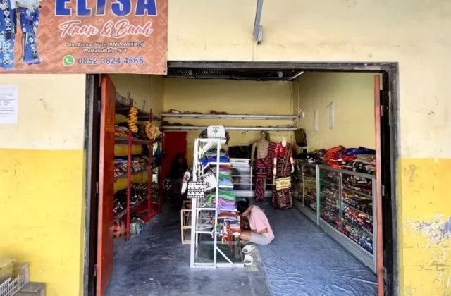 The entrance to Elisa Store reveals a person kneeling amidst vibrant Ikat Sumba textiles displayed on shelves and mannequins, under a banner.