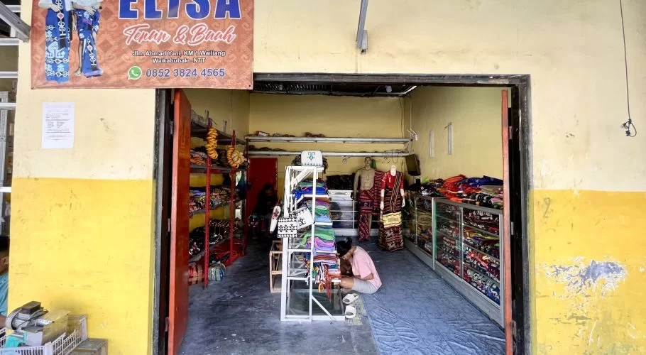 The entrance to Elisa Store reveals a person kneeling amidst vibrant Ikat Sumba textiles displayed on shelves and mannequins, under a banner.