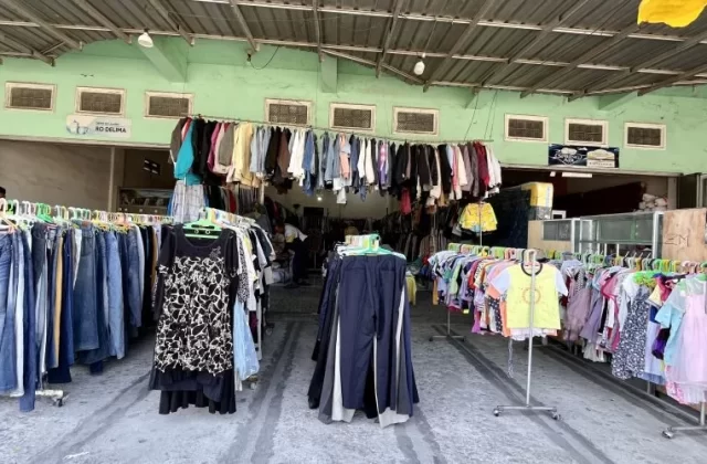 Inside the Gajah Mada thrift store in Waikabubak, numerous racks of colorful second-hand clothing are displayed under a corrugated metal roof and light green walls.