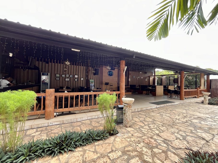 The exterior of HF Restaurant in Tambolaka, Sumba, features a covered patio with wooden pillars, string lights, tables, and a bar area where a person is visible.