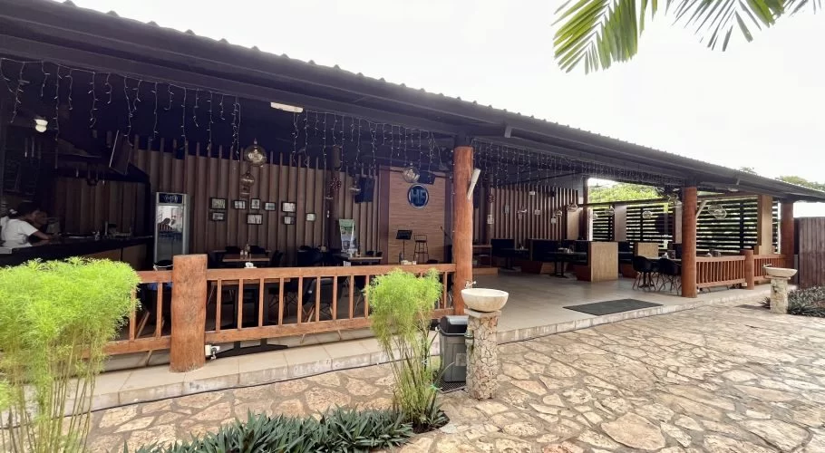 The exterior of HF Restaurant in Tambolaka, Sumba, features a covered patio with wooden pillars, string lights, tables, and a bar area where a person is visible.