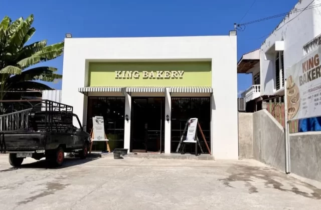 The white and light green exterior of King Bakery in Waingapu is visible under a clear blue sky, with a black pickup truck parked on the left.