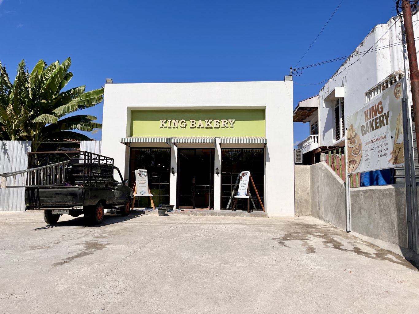 The white and light green exterior of King Bakery in Waingapu is visible under a clear blue sky, with a black pickup truck parked on the left.
