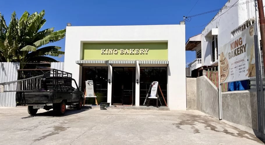 The white and light green exterior of King Bakery in Waingapu is visible under a clear blue sky, with a black pickup truck parked on the left.