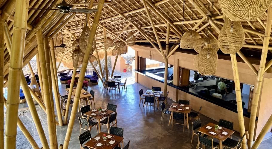 The spacious interior of Makan Dulu restaurant features a high, vaulted bamboo and thatched roof, with woven pendant lights above dining tables.