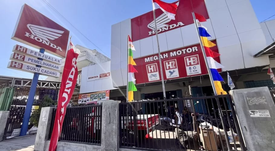 The red and white Megah Dealer Honda building in Waingapu, Sumba, displays Honda logos, flags, and a sign for sales, service, and parts.