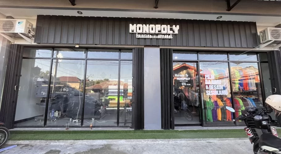 Monopoly Printing + Apparel storefront in Waingapu, with a dark grey facade, white sign, and glass windows displaying colorful apparel.