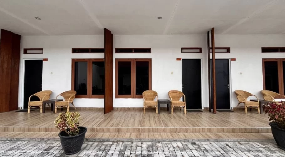 The white facade of Morika Inn Hotel features multiple rooms with dark doors and windows, each with a tiled porch and wicker seating.
