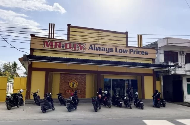 A vibrant yellow MR. DIY store with "Always Low Prices" signage stands under a partly cloudy sky, with numerous motorcycles parked in front.