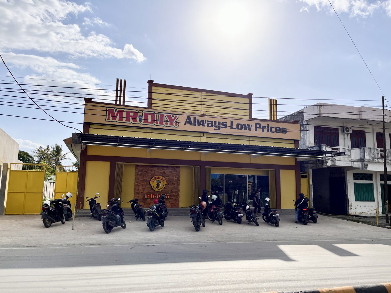 A vibrant yellow MR. DIY store with "Always Low Prices" signage stands under a partly cloudy sky, with numerous motorcycles parked in front.