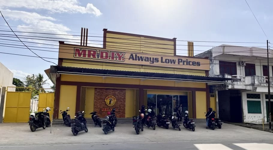 A vibrant yellow MR. DIY store with "Always Low Prices" signage stands under a partly cloudy sky, with numerous motorcycles parked in front.