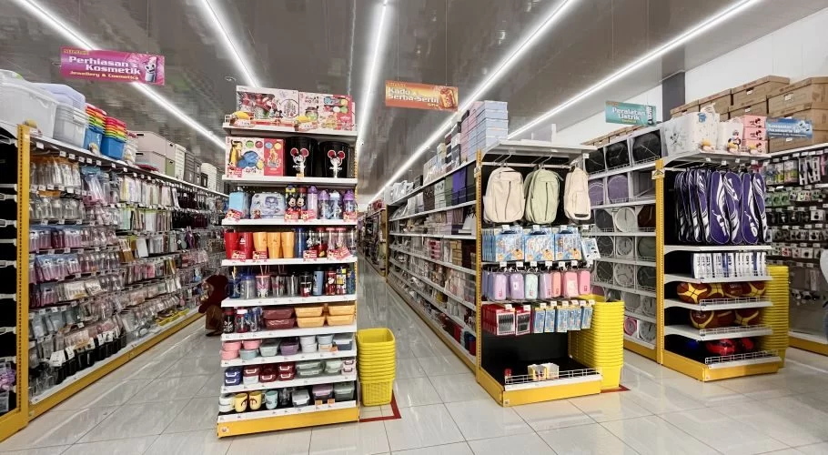 A brightly lit MR. DIY store interior in Tambolaka, Sumba, features long aisles of yellow-accented shelves stocked with diverse household goods.