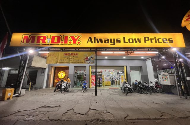 The brightly lit exterior of a MR. DIY store at night, featuring a large yellow sign and several motorcycles parked in front.