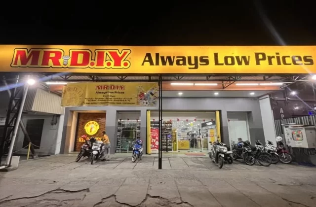 The brightly lit exterior of a MR. DIY store at night, featuring a large yellow sign and several motorcycles parked in front.