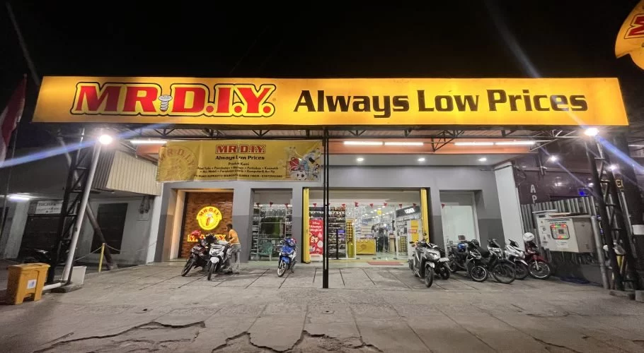 The brightly lit exterior of a MR. DIY store at night, featuring a large yellow sign and several motorcycles parked in front.