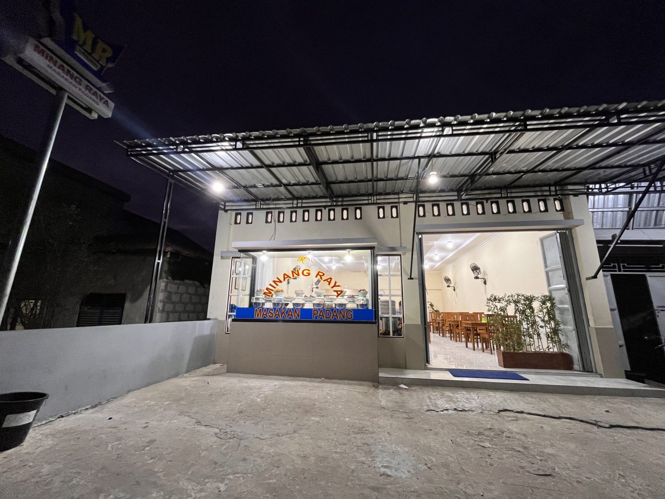 The brightly lit exterior of MR Restaurant in Tambolaka, Sumba, shows its open entrance, a food display counter, and an inviting dining area at night.