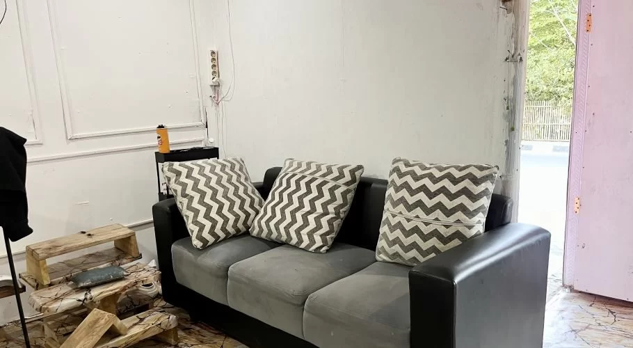 A cozy salon waiting area features a dark grey sofa with three chevron cushions against white walls, with an open doorway revealing a street.