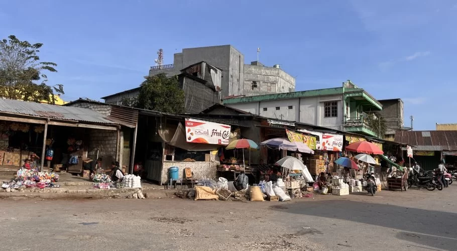 Numerous vendors sell various goods under colorful umbrellas along a bustling street at Pasar Inpres market in Waikabubak, Sumba.