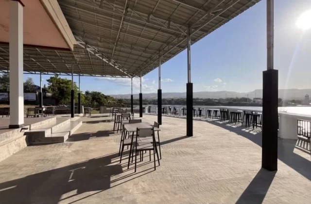 A large, covered outdoor dining terrace at Permata Restaurant overlooks the sunny port and ocean in Waingapu, Sumba, with tables and chairs.
