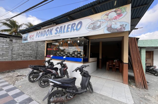 The exterior of Pondok Salero restaurant in Waikabubak features a white sign with blue text, a corrugated roof, and parked motorbikes under a bright sky.
