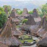 Prai Ijing traditional village in Sumba, Indonesia, shows many conical thatched-roof houses and stone megaliths amidst green trees.