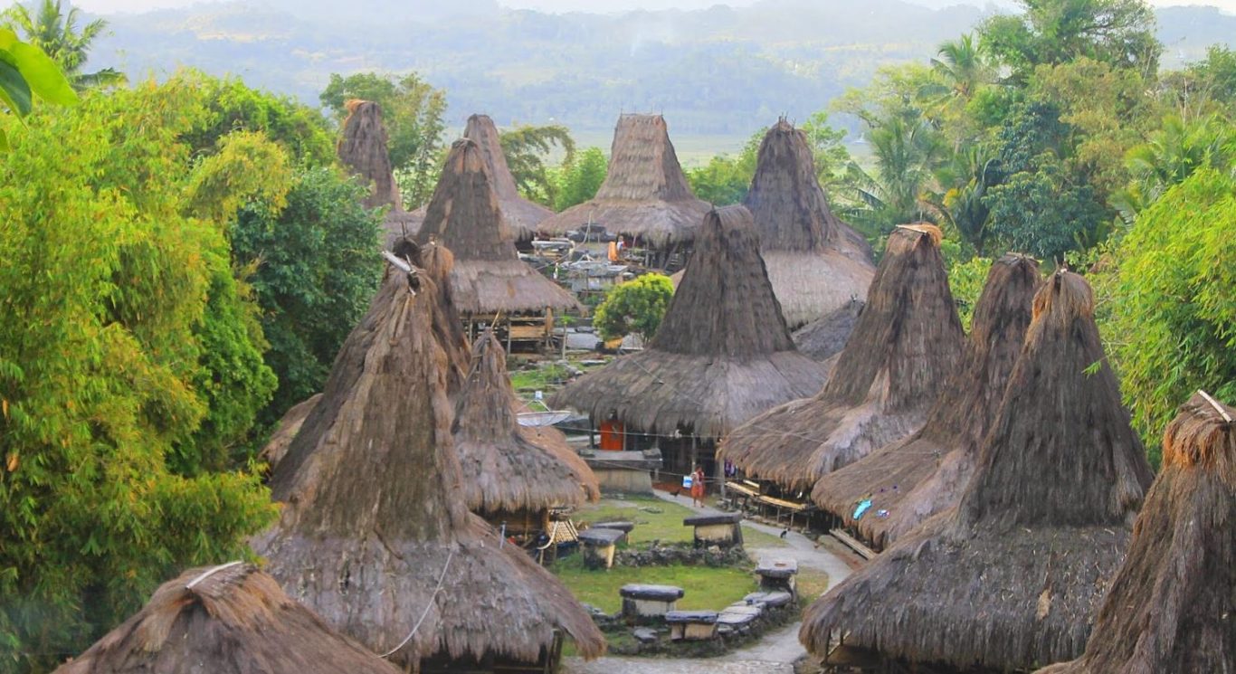 Prai Ijing traditional village in Sumba, Indonesia, shows many conical thatched-roof houses and stone megaliths amidst green trees.