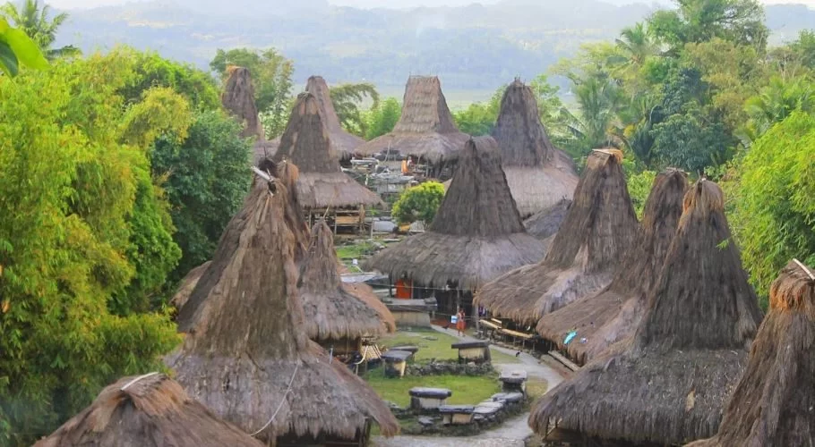 Prai Ijing traditional village in Sumba, Indonesia, shows many conical thatched-roof houses and stone megaliths amidst green trees.