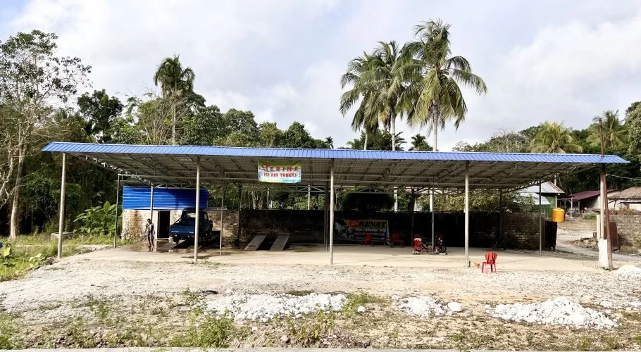A blue-roofed open-sided structure houses the Renata water provider and car wash, with a blue truck on a ramp and lush tropical trees in the background.